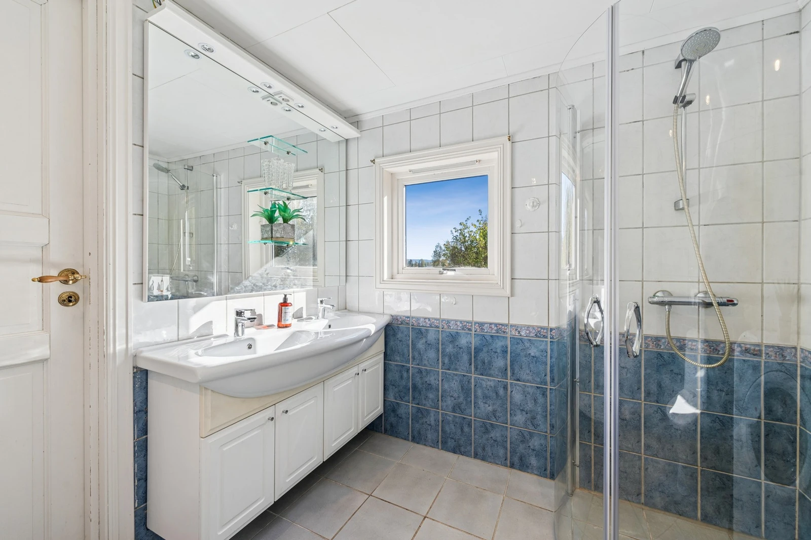 Badet er utstyrt med fliser på gulv og vegger, dobbelservant med underskap, speil med belysning og dusjhjørne. Galleribilde