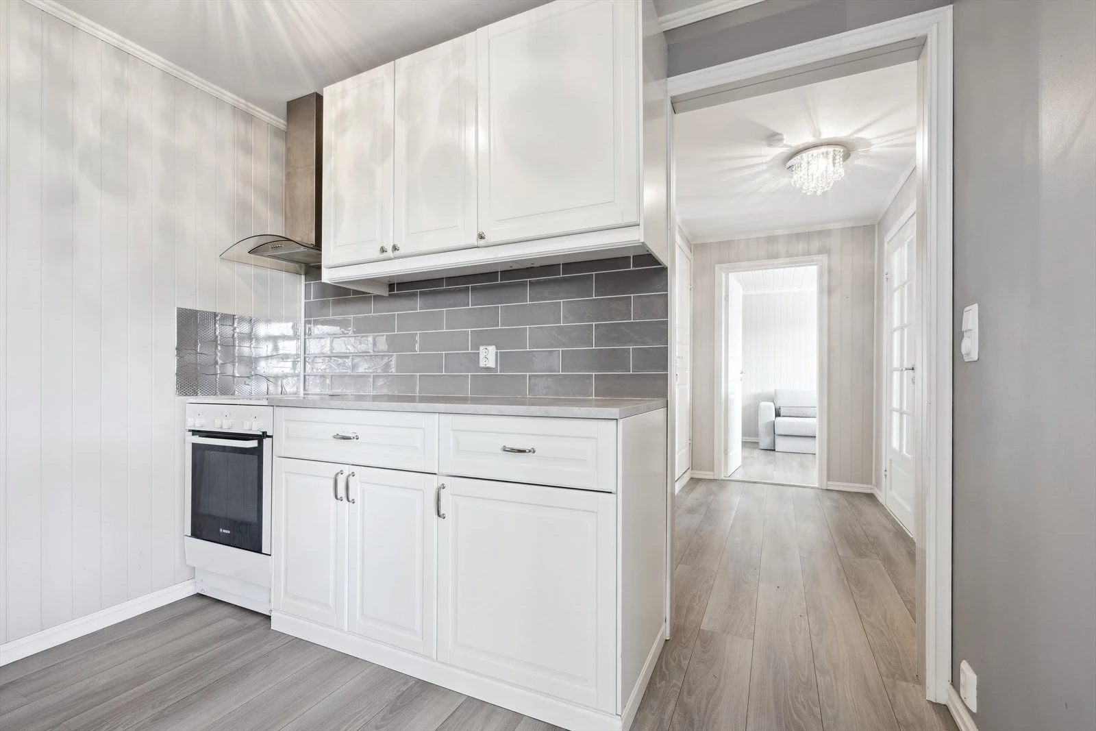 Pent kjøkken med profilerte fronter og fliser over benk