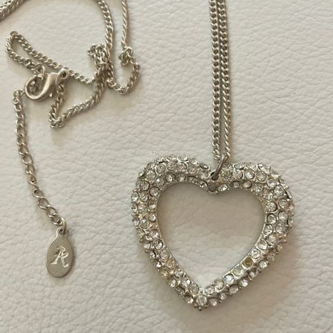 Langt sølvfarget halskjede med stort hjerteanheng med krystaller.