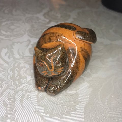 Katt i håndlaget keramikk orange og brun med små nagg på ene øret og poten