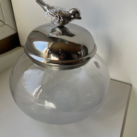 Glasskrukke med fugl i sølvfarge på lokket