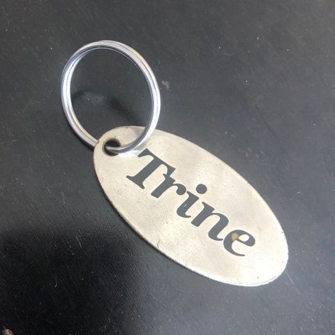 Nøkkelring med navnet Trine.  Mål: 6 x 3 cm.