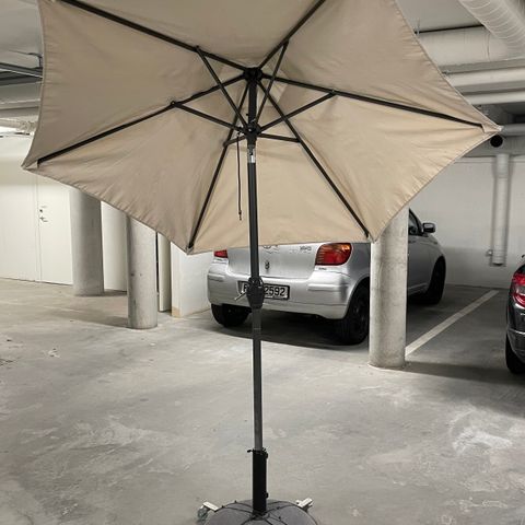 Beigefarget parasoll m/betong fot på hjul.