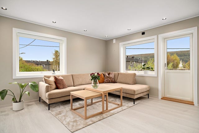 Rommet har moderne overflater med laminatgulv, malte vegger og innfelte downlights i himlingen, noe som gir et stilrent og helhetlig uttrykk. De store vindusflatene slipper inn rikelig med dagslys og bidrar til en luftig romfølelse.