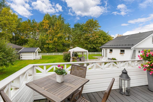 Verandaen byr på flere hyggelige sitteplasser med utsyn mot den frodige hagen og eiendommens garasje. Et flott uterom for både morgenkaffen 