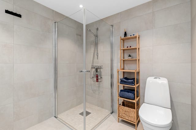 Badet er pent og moderne med lyse fliser og dusjhjørne.