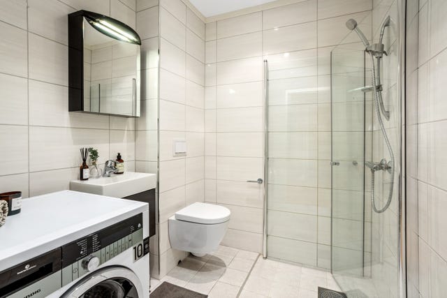 Badet har dusjhjørne med dører, vegghengt dusjarmatur og vegghengt toalett. Det er også opplegg for vaskemaskin