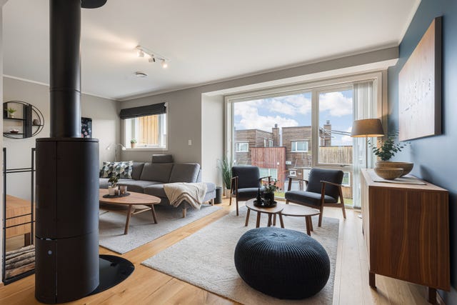 En innbydende og stilren stue med store vindusflater som slipper inn rikelig med dagslys. Vedovnen tilfører både varme og en lun atmosfære.