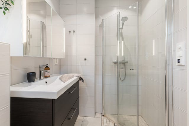 En romslig dusjsone med glassvegger og moderne dusjgarnityr gir badet et stilrent og tidløst uttrykk. Gulvvarme sørger for ekstra komfort i 