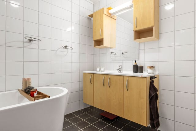 Badet holder en moderne og stilren standard med hvite fliser på vegg og mørke på gulv.