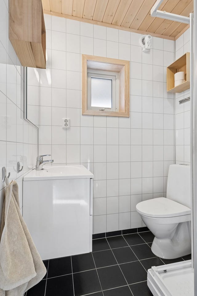 Badet er innredet med dusjkabinett, gulvmontert toalett og enkel baderomsinnredning med nedfelt servant og speil med belysning.