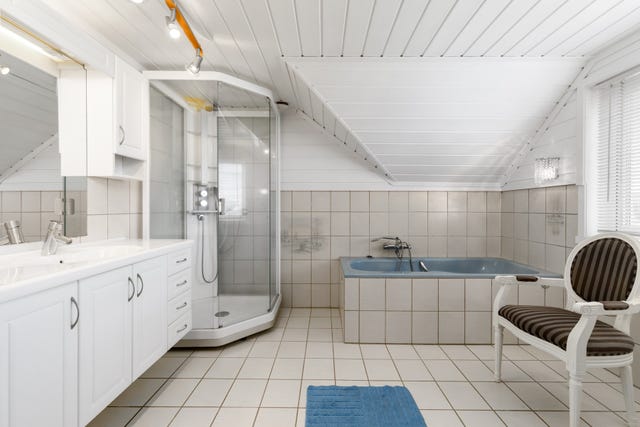 Badet i 2. etasje. Rommet er flislagt på gulv og vegger med badekar, dusjkabinett og vegghengt servantinnredning.