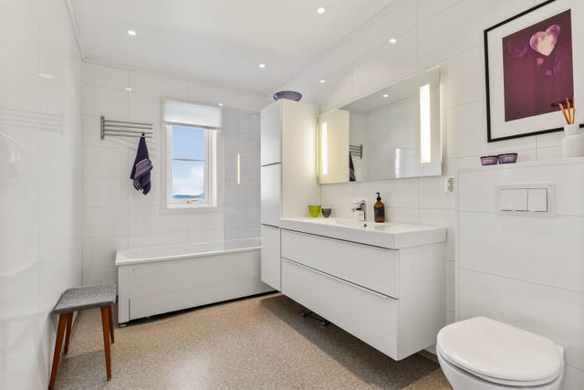 Badet fremstår lyst og moderne, med tidløse overflater og en romslig planløsning. Her er det badekar med veggmontert blandebatteri og dusjløsning, noe som gir fleksibilitet både for barnefamilier og for den som setter pris på et varmt bad.