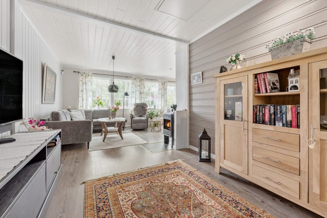 Her ser du fra den indre del av stua (som tidligere var soverom) mot vinduer og dør ut til veranda.  Koselig med vedovn i sonen mellom de to stuedelene.