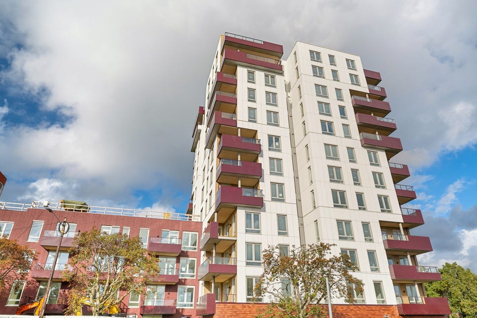 Tårnet har lys fasade og balkonger i rødt; lamellbygget ligger inntil.