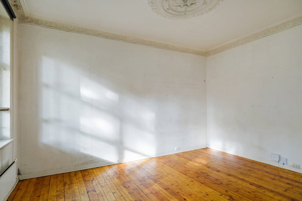 Stuen har tregulv og store veggflater. Tilstandsrapporten beskriver betydelig slitasje på overflatene og behov for omfattende sanering.