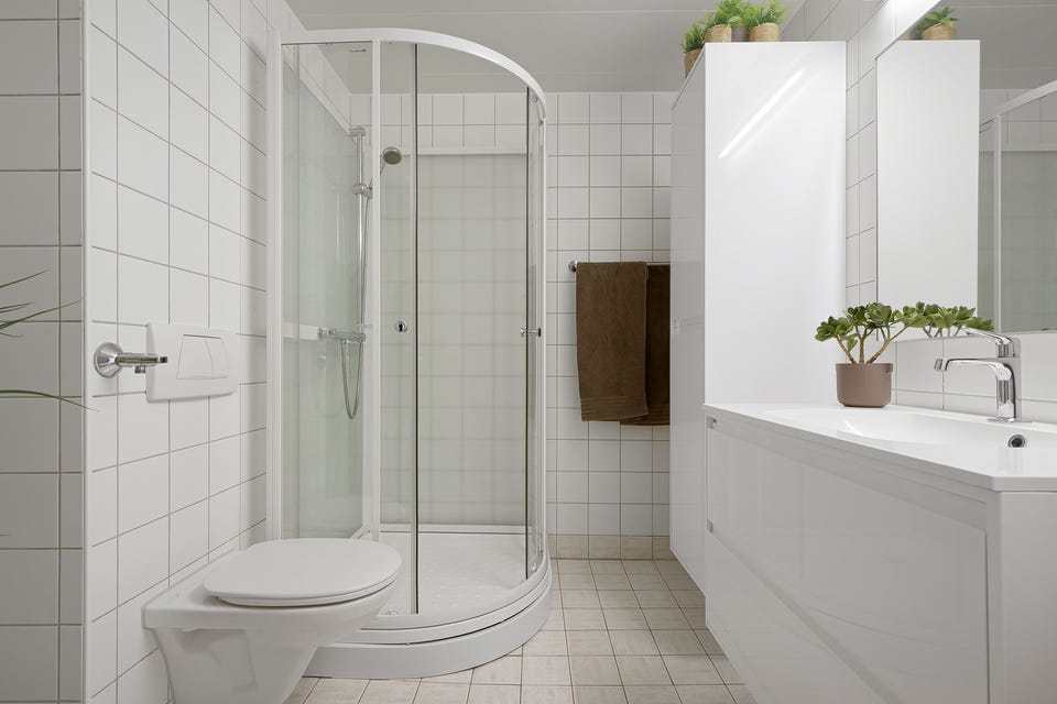 Badet inneholder vegghengt servantskap med heldekkende servant og ett-greps armatur, speil, overlys og stikkontakt over servant, dusjkabinett, toalett og opplegg for vaskemaskin.