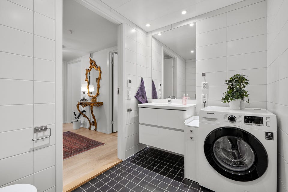 Leiligheten har et lyst flislagt baderom fra byggeåret 2021. Moderne baderomsinnredning med skuffer og heldekkende servant, stort innfelt speil over. I hjørnet er det plass og opplegg for vaskemaskin, samt tørketrommel over om ønskelig.