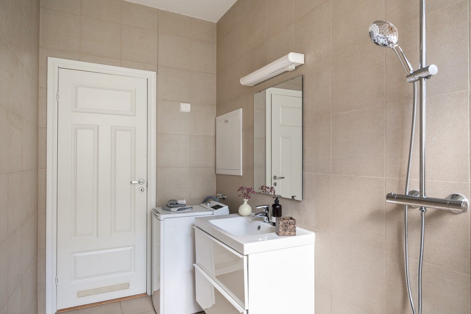 I hjørnet er det plass og opplegg for vaskemaskin. Baderommet har delikate fliser på gulv og vegger, elektriske varmekabler, downlights i himlingen og balansert ventilasjon (Villavent).