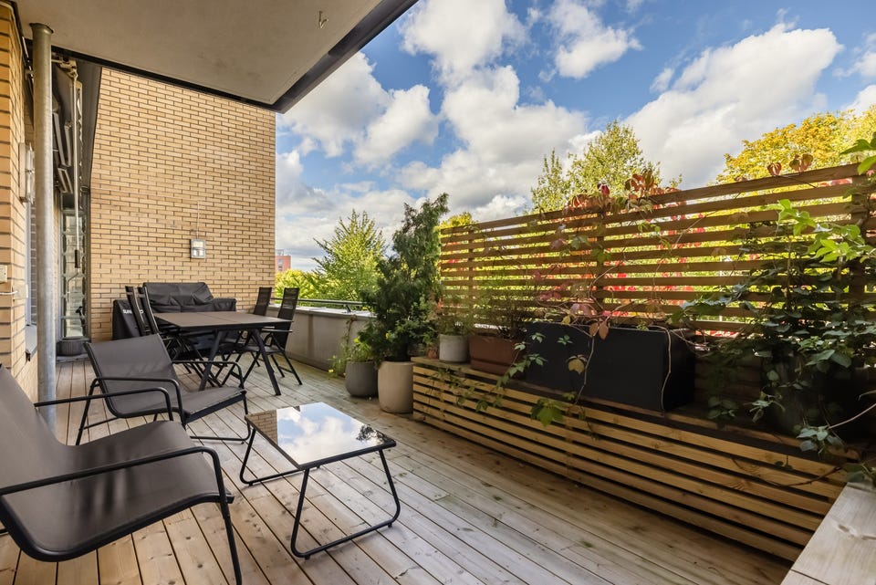 Balkongen er delvis overbygget, har terrassebord på gulv og en fin plassbygget sittebenk med levegg.