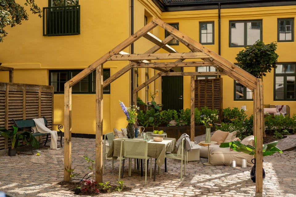 Pergola og brostein i borettslagets felles gårdsrom. De avgrensede terrassene langs fasaden tilhører andre leiligheter.