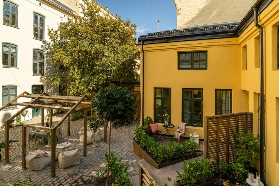Oversikt over felles gårdsrom med pergola og gangarealer. Andel 16 har tilgang til fellesarealene, men ingen privat terrasse.