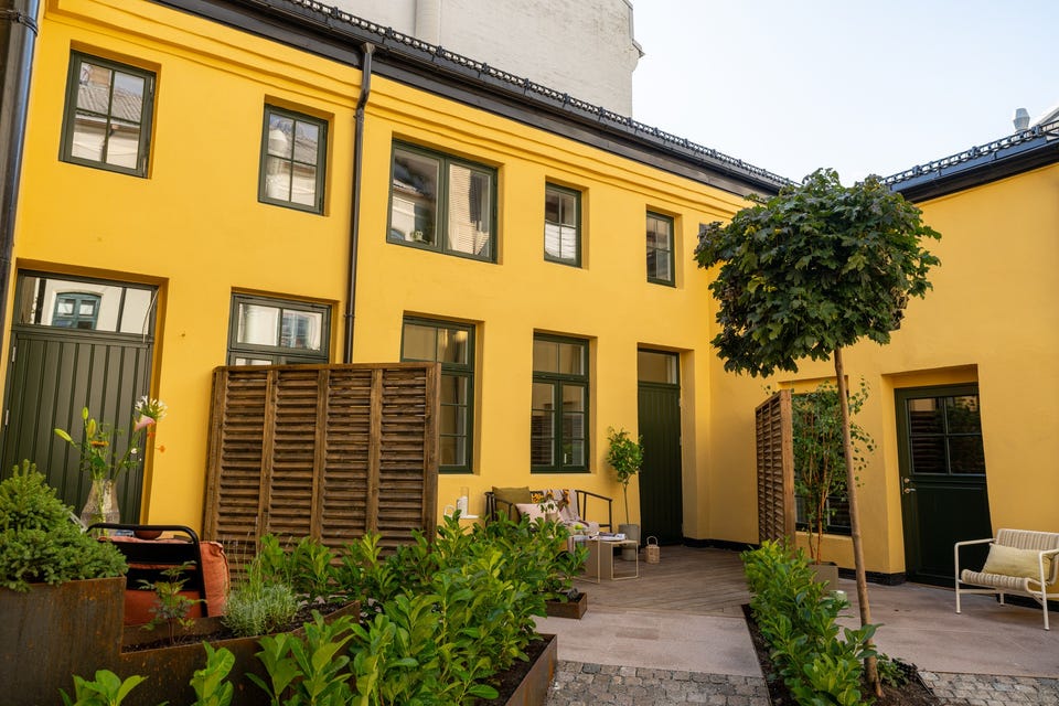 Den gule bakgårdsfasaden omkranser felles gårdsrom. De avgrensede terrassene på bakkeplan tilhører andre leiligheter.