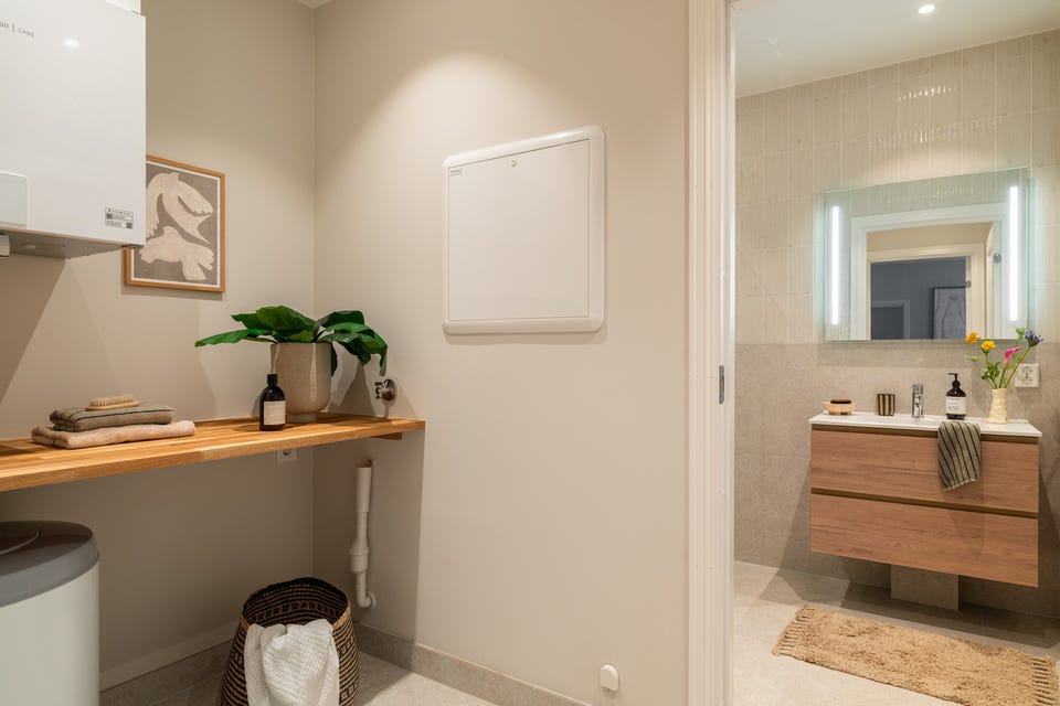 Eget vaskerom/bod med opplegg for vaskemaskin og plass til oppbevaring, praktisk plassert ved badet.