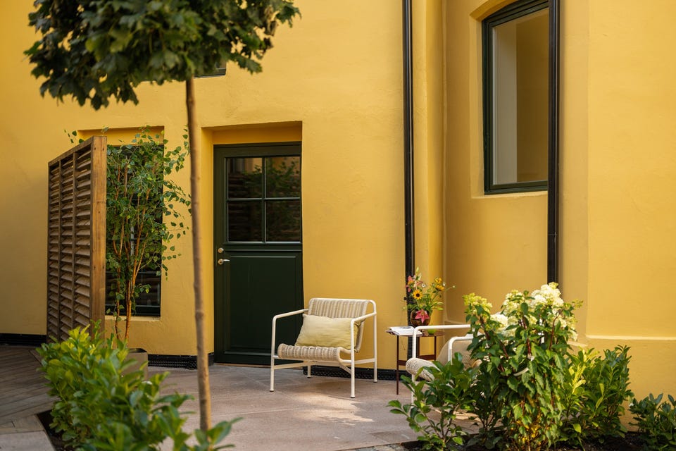 Beplantning og den gule murfasaden rammer inn terrassearealet som denne leiligheten har eksklusiv bruksrett til.