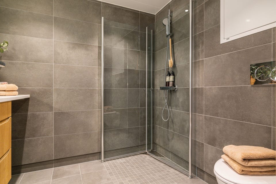 Badet har dusjsone med glassvegger og et helhetlig flislagt uttrykk. Gulvvarmen kan styres med boligens xComfort-system.