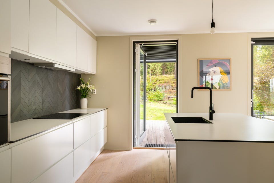 Innredningen har hvite glatte fronter og laminert benkeplate med planlimt oppvaskkum og sort armatur med uttrekkbar tut.