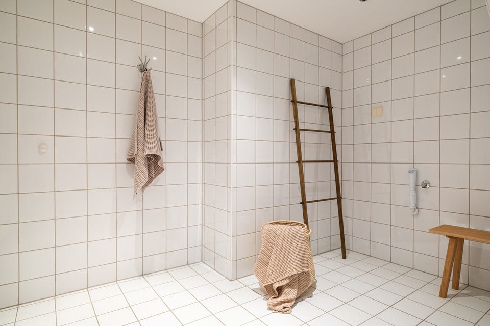 I hjørnet er det plass og opplegg for vaskemaskin. Baderommet har hvite fliser på gulv og vegger, vannbåren gulvvarme, downlights i himlingen