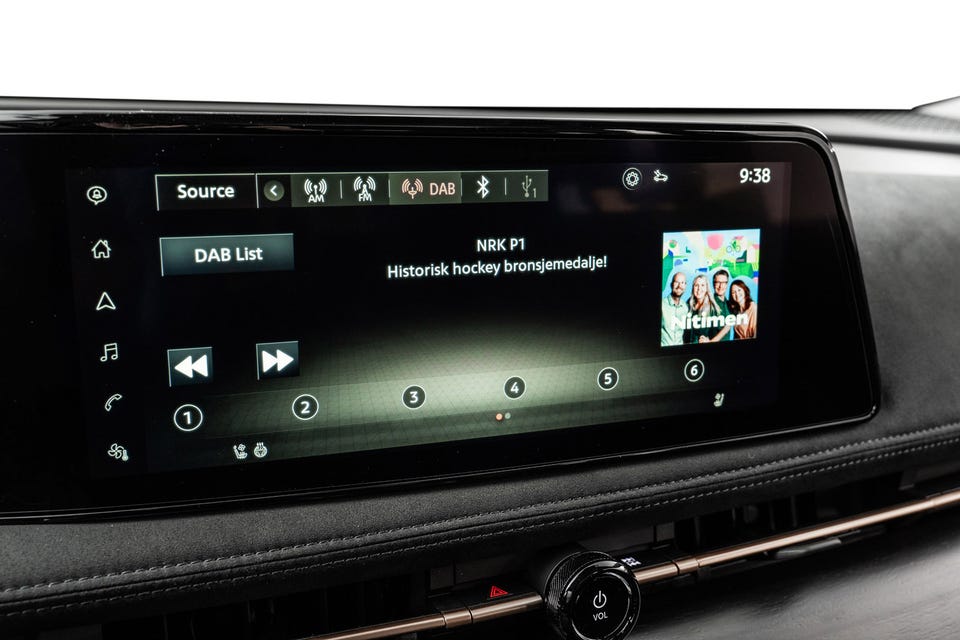 Bred infotainmentskjerm med DAB-radio, mørkt interiørpanel med kopperdetaljer og fysisk volumknapp