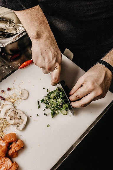Kokk med skjærebrett kutter opp ingredienser til mat.