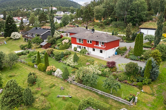 Dronofoto tomt og fasade med Brannhaugen i bakgrunn.