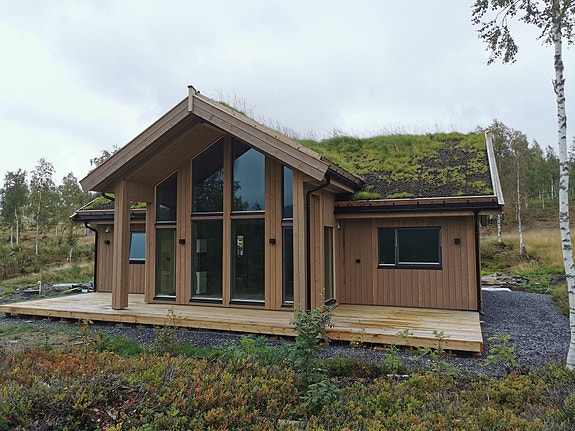 Fasadebilde. Stor terrasse i hele hyttas lengde og nylagt torv på taket.