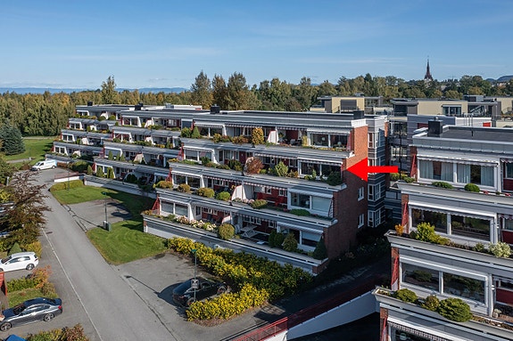 Dronefoto fasade, nest øverste etasje. Leilighetens plassering markert med rød pil.
