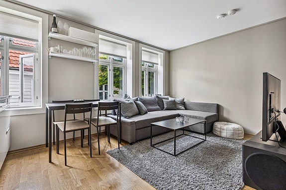 Lys og fin stue med god takhøyde. Stuen er innredet med sofa, kjøkkenbord og stoler.