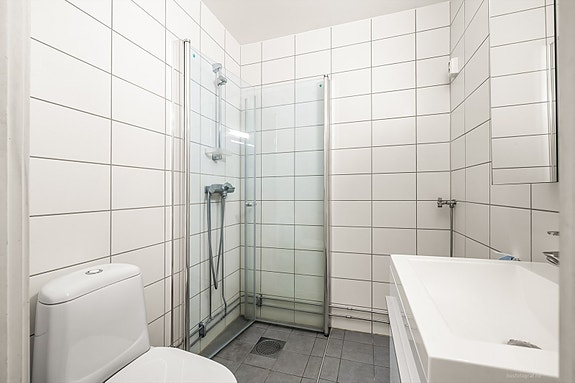 Pent flislagt bad med innredning bestående av klosett, dusjhjørne og baderomsinnredning med speilskap.