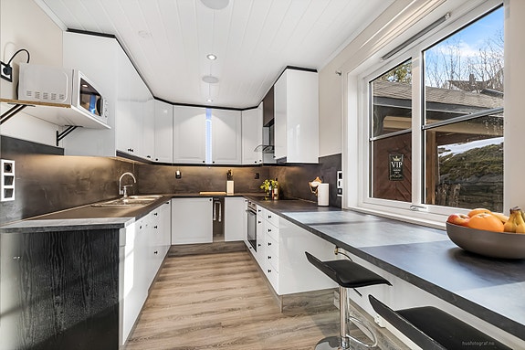 Stilrent og moderne kjøkken med integrerte hvitevarer, god arbeidsflate og store vinduer som gir rikelig med dagslys.