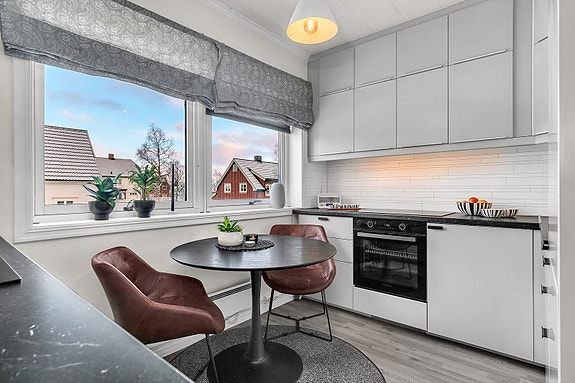 Pent kjøkken med plass til spisegruppe foran vindu. Kjøkkenet har innredning med glatte fronter.