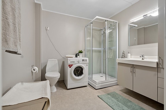 Badet er innredet med dusjkabinett, toalett, servant med oppbevaring og opplegg for vaskemaskin - alt du trenger i hverdagen