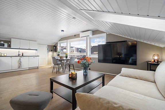 Rommet oppleves åpent og sosialt, med fin flyt mellom sittegruppe, spiseplass og kjøkken. Store vinduer slipper inn rikelig med dagslys