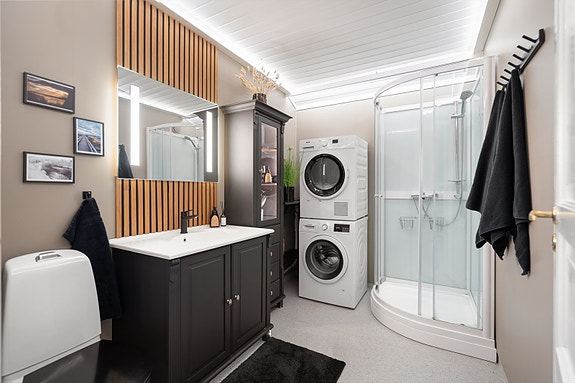 Stilrent bad med dusjkabinett, toalett og moderne servantinnredning. De varme tonene kombinert med paneldetaljer i tre gir rommet et elegant og lunt uttrykk