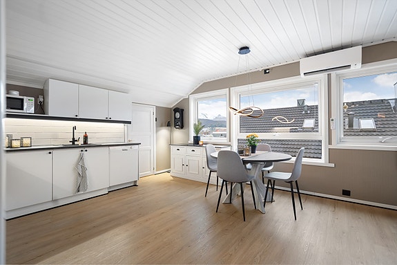 Pent kjøkken med god benkeplass og tidløs innredning i hvitt. Praktisk planløsning og integrert belysning under overskapene