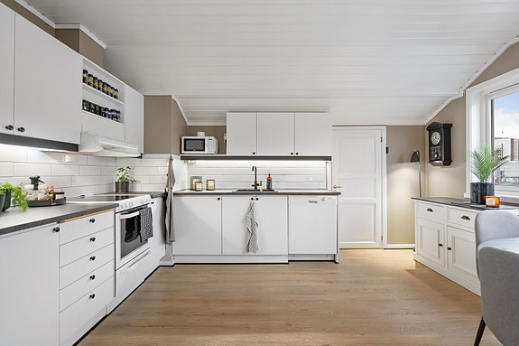 Lyst og innbydende kjøkken med moderne uttrykk og rene linjer. Her får du god benkeplass, praktisk planløsning og integrert belysning som gir et lunt arbeidslys