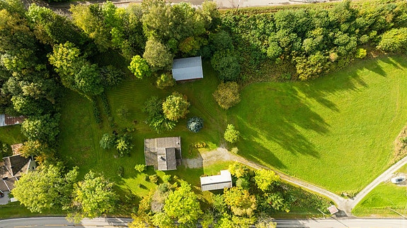 Oversiktsbilde som viser hus, uthus og hage i idylliske omgivelser.