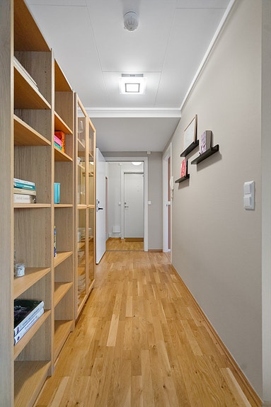 Fra gangen åpner leiligheten seg mot de øvrige rommene. De lyse flatene og parkettgulvet gir et helhetlig og