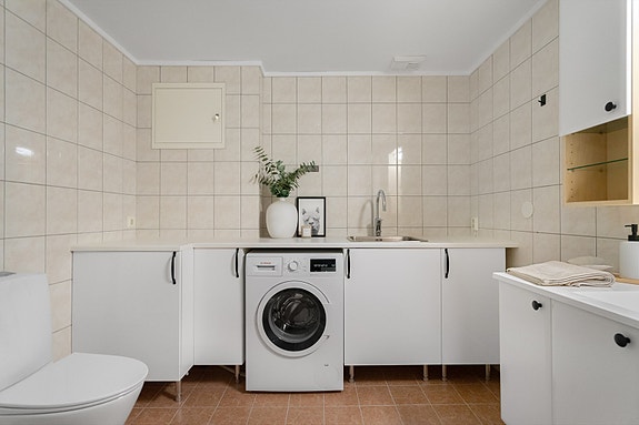 Romslig bad med lyse fliser og praktisk innredning som gir godt med benkeplass og oppbevaring