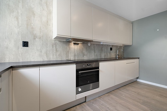 Kjøkken i delikate fargetoner med slette fronter, mørk benkeplate og praktisk planløsning - et rom som inviterer til matlaging og trivsel